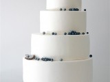 a minimalist coastal wedding cake in white decorated with blue edible pearls and a pearl in a shell on top