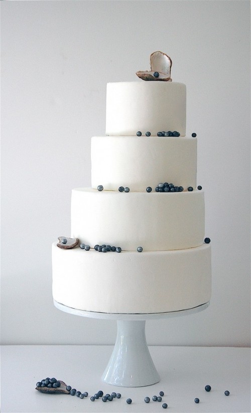 a minimalist coastal wedding cake in white decorated with blue edible pearls and a pearl in a shell on top