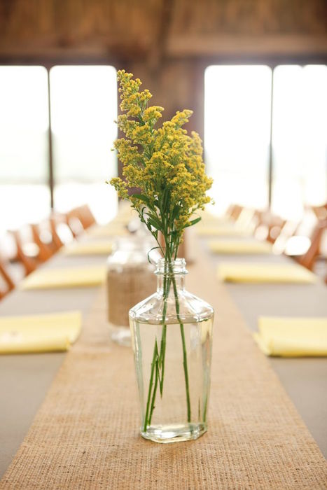 a minimalist wedding tablescape with bright napkins and a woven table runner plus some blooms in a bottle