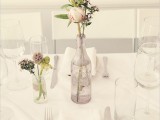 a minimalist neutral table setting with a blush bottle with blooms and greenery and a jar with an arrangement