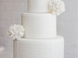 a minimalist white wedding cake with a plaid pattern and white blooms will complete the wedding theme
