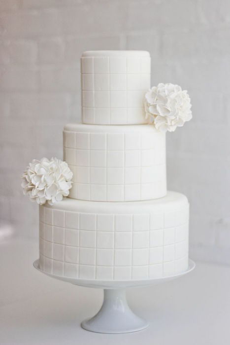 a minimalist white wedding cake with a plaid pattern and white blooms will complete the wedding theme