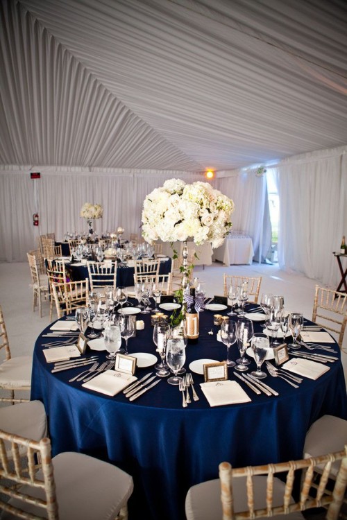 a refined navy and white tablescape with a navy tablecloth, a lush white floral centerpiece and some elegant cutlery