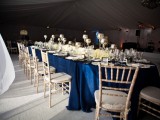 a refined nautical tablescape with a navy tablecloth, neutral floral centerpieces, candles and white chairs