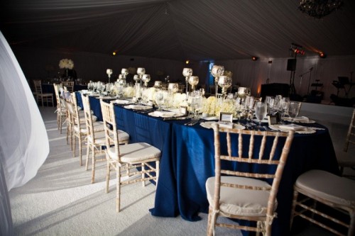 a refined nautical tablescape with a navy tablecloth, neutral floral centerpieces, candles and white chairs
