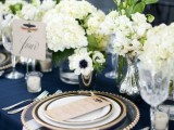 an elegant tablescape with a navy tablecloth, white florals for a centerpiece, gold edge plates and silver
