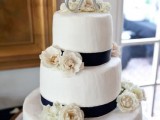 a white textural wedding cake with navy ribbons, neutral blooms, a metallic topper