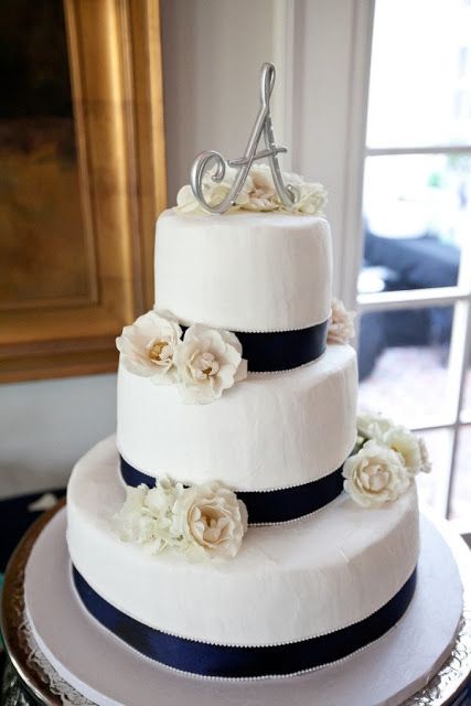 a white textural wedding cake with navy ribbons, neutral blooms, a metallic topper