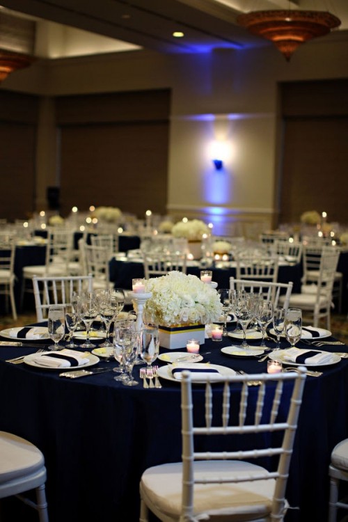 a chic contrasting tablescape with a navy tablecloth, a white floral centerpiece and candles and neutral napkins