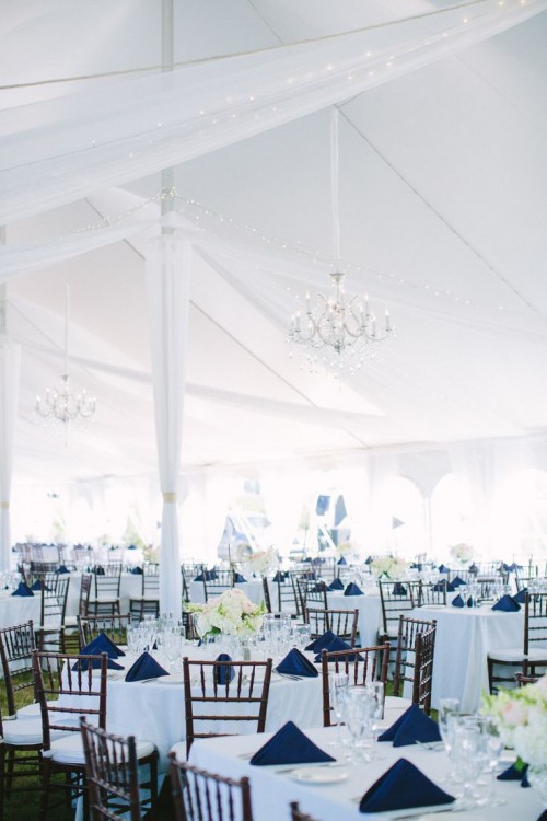 a chic navy and white tablescape with a white tablecloth, navy napkins, neutral blooms and refined crystal chandeliers