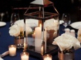 an elegant navy wedding table setting with a large candle lantern, white rose arrangements and candles all around