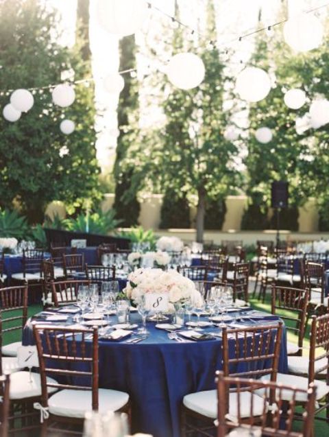 a bold table setting with a navy tablecloth, a neutral floral centerpiece and white paper lamps over the space