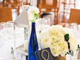 a gorgeous nautical wedding tablescape with a striped table runner, white blooms in a blue bottle, a rope table number and a rope wrapped vase