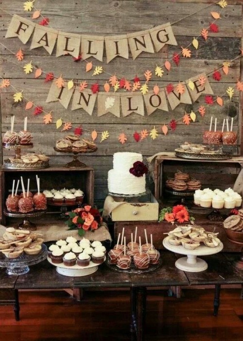 a fall dessert table with burlap garlands, bright leaf garlands, crates and a wooden table for serving food
