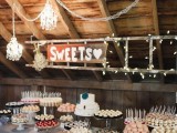 a chic wedding dessert table with lights, elegant chandeliers, a rustic sign and a table with lots of sweets