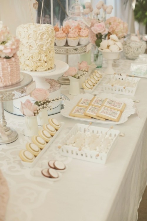 a white and blush wedding dessert table with blush roses and tasty romantic sweets in simple white porcelain