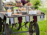 a rustic cart wedding dessert table with a colorful banner, stands with sweets and bright blooms in vases