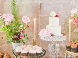 a wedding dessert table with lots of blooms, candles, greenery and simple plates and stands for sweets