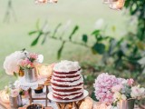 a summer weddign dessert table with pendant candle lanterns, pink blooms and greenery, pies and cakes on stands and folding stands