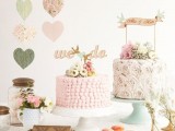 a chic vintage wedding dessert table with pastel heart banners, pink and white blooms and greenery, pink cakes and macarons