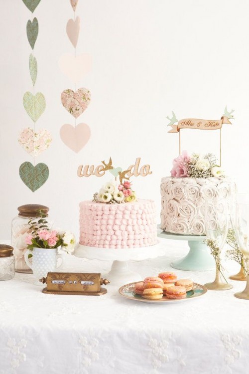 a chic vintage wedding dessert table with pastel heart banners, pink and white blooms and greenery, pink cakes and macarons