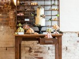 a rustic dessert table with a stand with bright macarons, blooms and greenery and a cake on a chic black stand