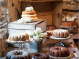 a rustic wooden dessert table with crates and a variety of bundt cakes and naked ones plus blooms around