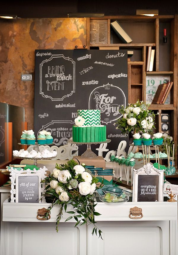 A bright green or emerald wedding dessert table with white flowers and greenery and tall stands for yummies