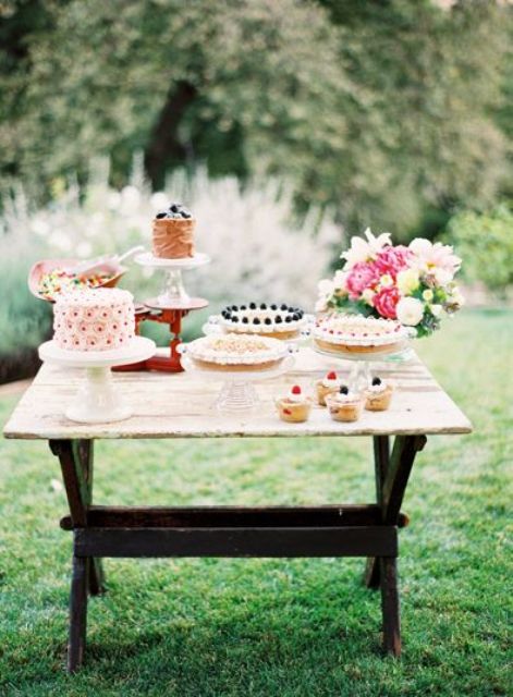 a bright summer dessert table with colorful blooms and greenery, tasty and delicious sweets and petals