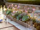 a long wedding centerpiece with a wooden box planter, several kinds of succulents, pink blooms and some greenery
