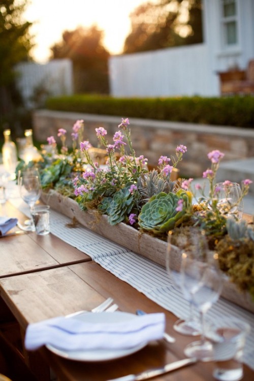 a long wedding centerpiece with a wooden box planter, several kinds of succulents, pink blooms and some greenery