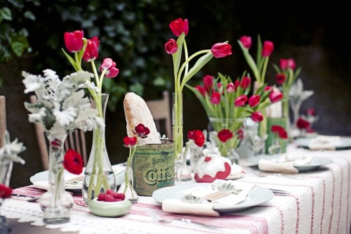 a relaxed summer tablescape with a striped tablecloth, bright red tulips and pale greenery in vases