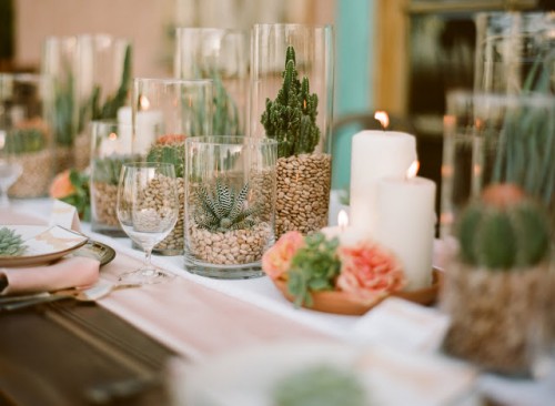 a summer wedding tablescape done with potted cacti, candles and peachy blooms plus light pink linens