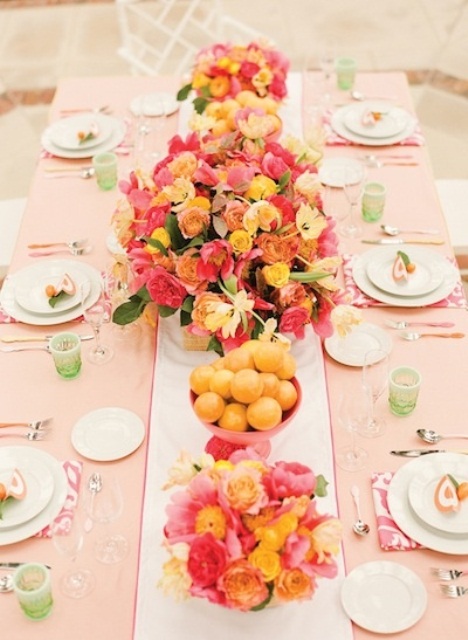 a pastel summer wedding tablescape with a peachy tablecloth, bright linens, green glasses and super bold summer florals and fruits