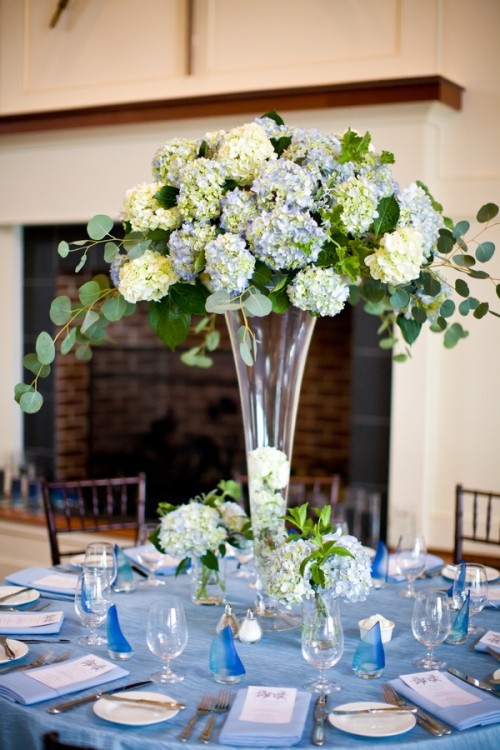 a beautiful summer wedding tablescape with a blue tablecloth, blue linens and lush blue and white oversized floral centerpiece
