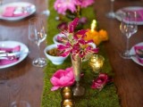 a summer wedding tablescape with a moss table runner, bright blooms, candles and purple linens