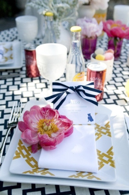 a bright summer wedding tablescape with printed linens, a pink bloom, candles, a card with a striped bow