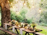 a woodland summer wedding tablescape with bulbs over it, with dark blooms, greenery and ferns and neutral linens