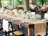 a rustic summer wedding tablescape with a burlap runner and neutral linens, pastel and white blooms and gorgeous crystal chandeliers over the space