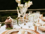 a neutral rustic wedding tablescape with wooden chargers, neutral blooms, antlers and moss for a summer woodland wedding