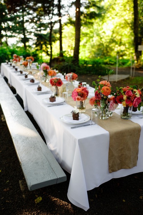 a bright summer wedding tablescape with a burlap table runner, bright blooms, favor boxes and a white table runner