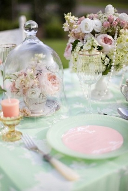 a chic pastel wedding tablescape with light green and pink plates, linens, blooms and peachy candles plus pearl strands