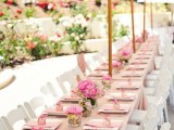 a pastel pink summer wedding tablescape with pink linens, bright blooms, favor boxes and umbrellas over all the tables to prevent excessive sunshine