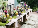 a bright whimsical tablescape for a summer woodland wedding, with a moss runner, bright florals and candle lanterns