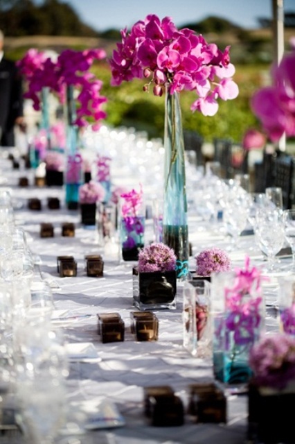 a super bold summer wedding tablescape with purple blooms in blue vases, candles in dark candleholders and all white everything to create a contrast