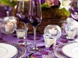 a colorful summer wedding tablescape with purple linens, purple and neutral blooms in moss, candles and purple glasses