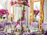 a bright and whimsical wedding reception space done with purple chairs, a large mirror, oversized lush florals and candles