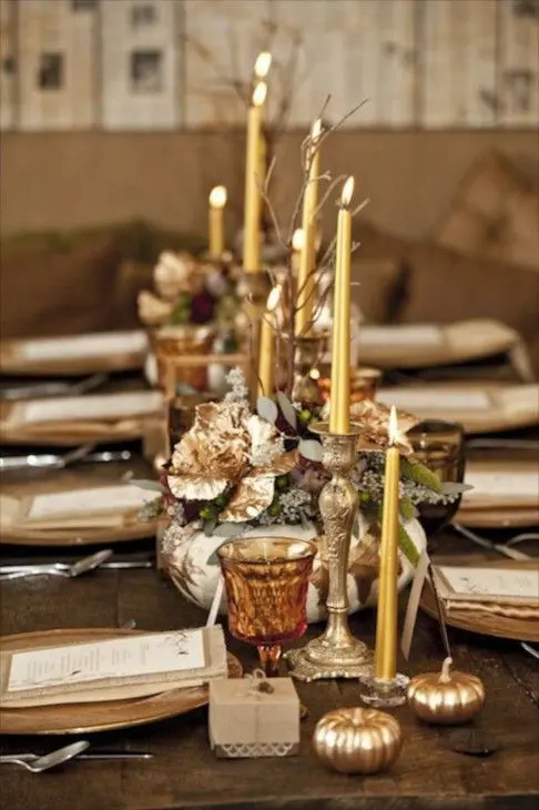 a chic and refined Thanksgiving tablescape with colored glasses, gilded candles, pumpkins and leaves, chargers and an uncovered table