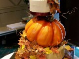a fall or Thanksgiving wedding cake with a tier covered with sugar leaves, a large pumpkin and a white wedding cake on top plus more sugar leaves
