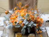 a bright fall or Thanksgiving centerpiece for a wedding composed of pale greenery, bold orange berries and fruits is a great idea for a harvest wedding